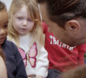 Deux enfants de maternelle, un adulte penche vers eux.